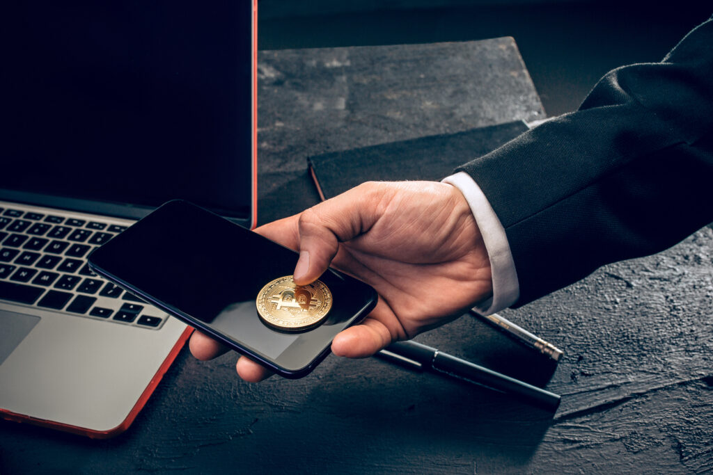 How to Add Money to Your Crypto Account: The golden bitcoin and mobile phone in male hands.