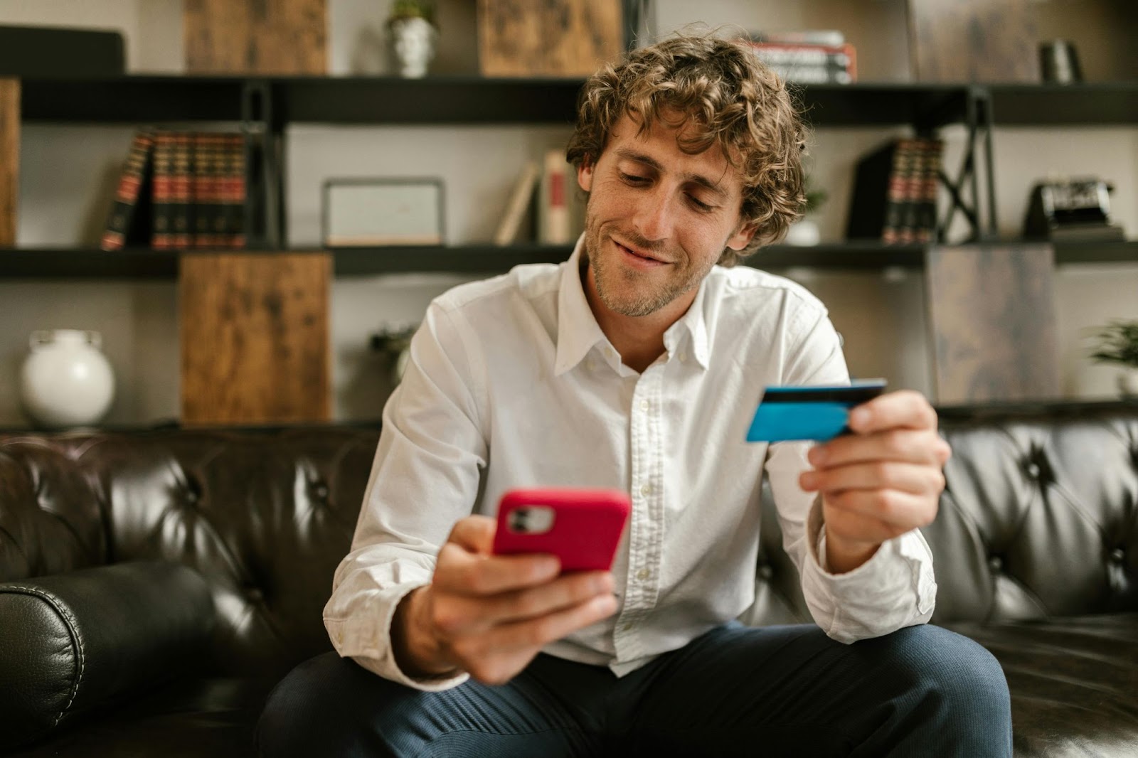 A man holding a debit card and smiling at this phone