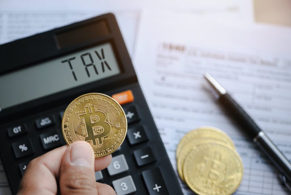 暗号通貨の課税を象徴する、税金が書かれた電卓、暗号通貨のコイン、納税申告書