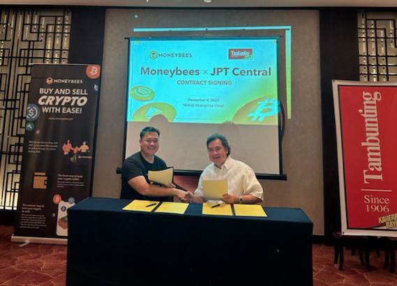 A snapshot of two men shaking hands while holding some documents during Tambunting and Moneybees partnership.