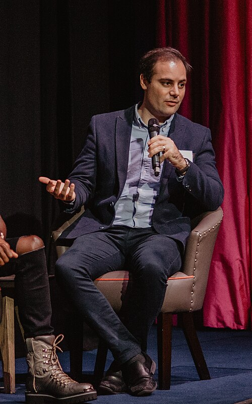 Ben delo holding a mic and speaking at an event