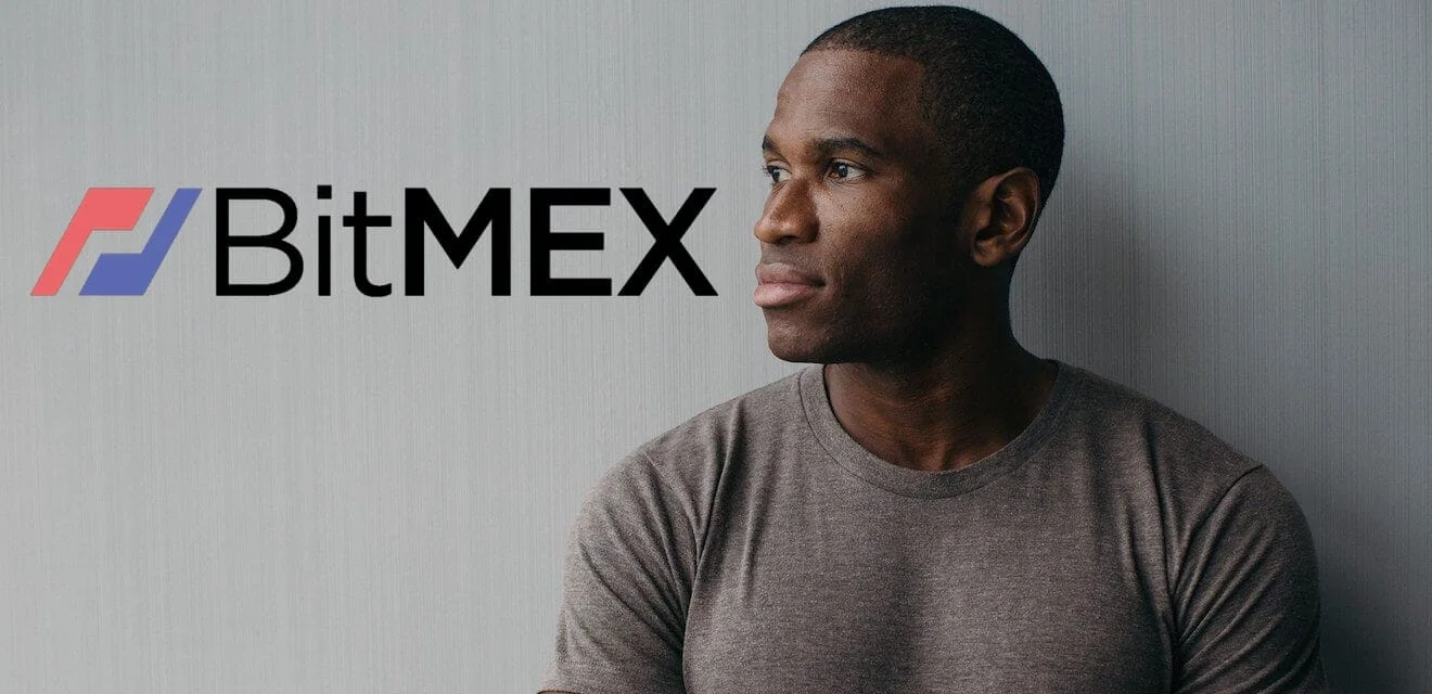 Porträt von Arthur Hayes, dem CEO von BitMEX, der neben dem BitMEX-Logo vor hellgrauem Hintergrund zur Seite blickt.
