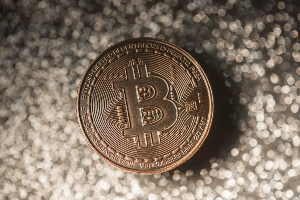Gold Bitcoin coin centered against a glittering, out-of-focus metallic background.