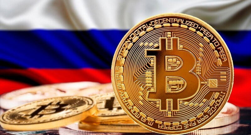 Gold Bitcoin coin displayed prominently in the foreground with the Russian flag in the background.