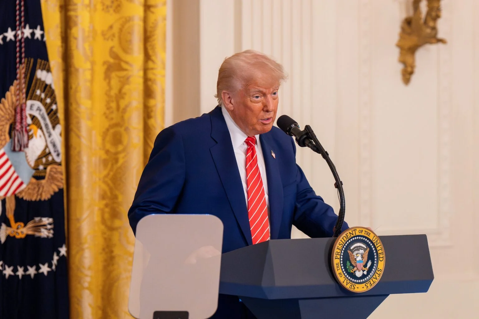 Donald Trump speaking at a podium bearing the Seal of the President of the United States during a formal address.