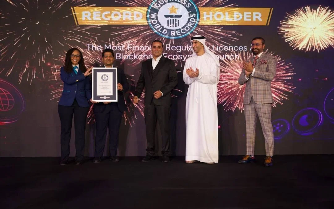 Five people stand on a stage during a Guinness World Records presentation, with one recipient holding an official Guinness World Records certificate. Fireworks graphics and a large screen displaying "Record Holder" form the backdrop.