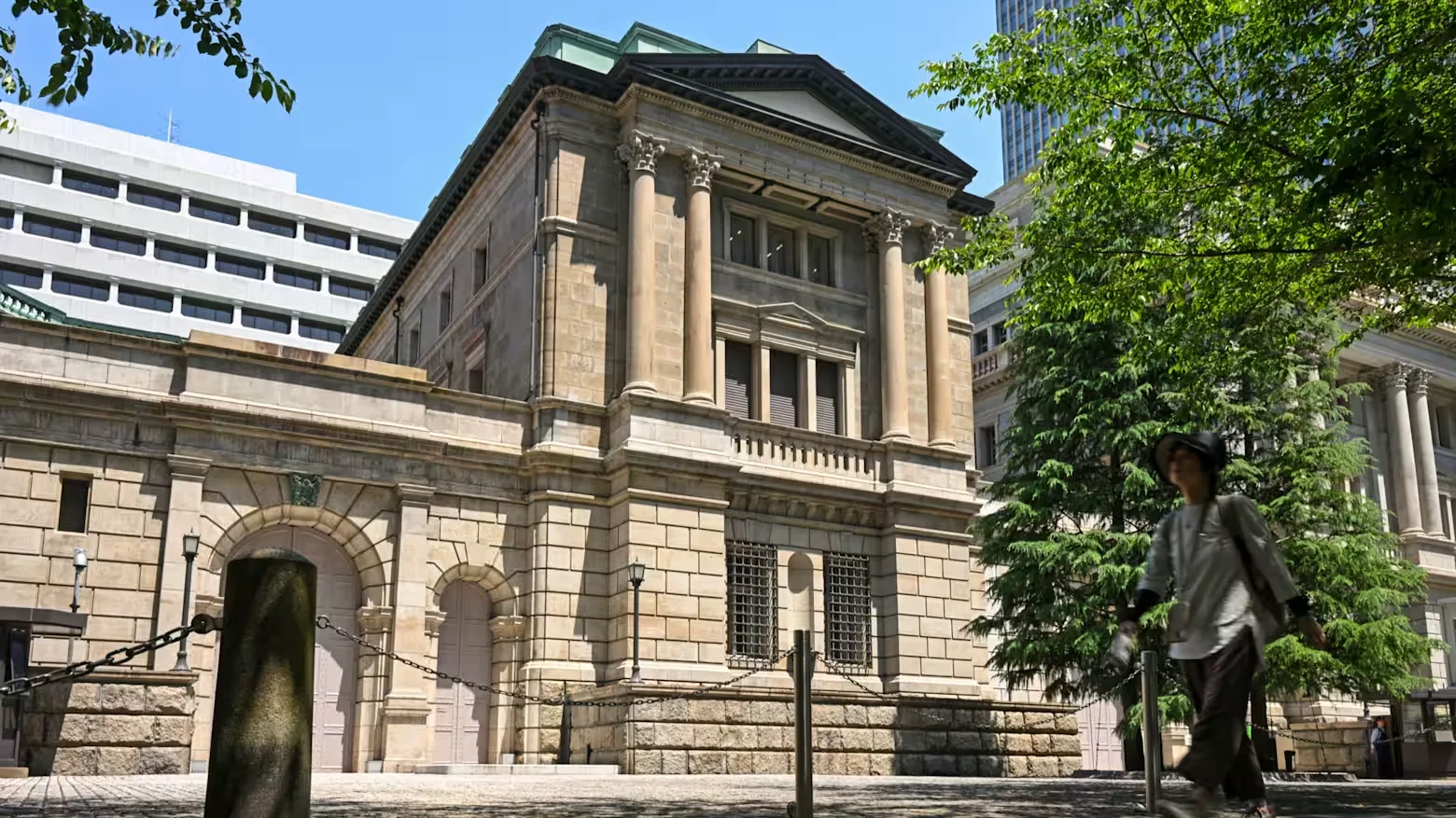 Bank of Japan headquarters building in Tokyo, Japan, surrounded by trees and nearby city buildings.