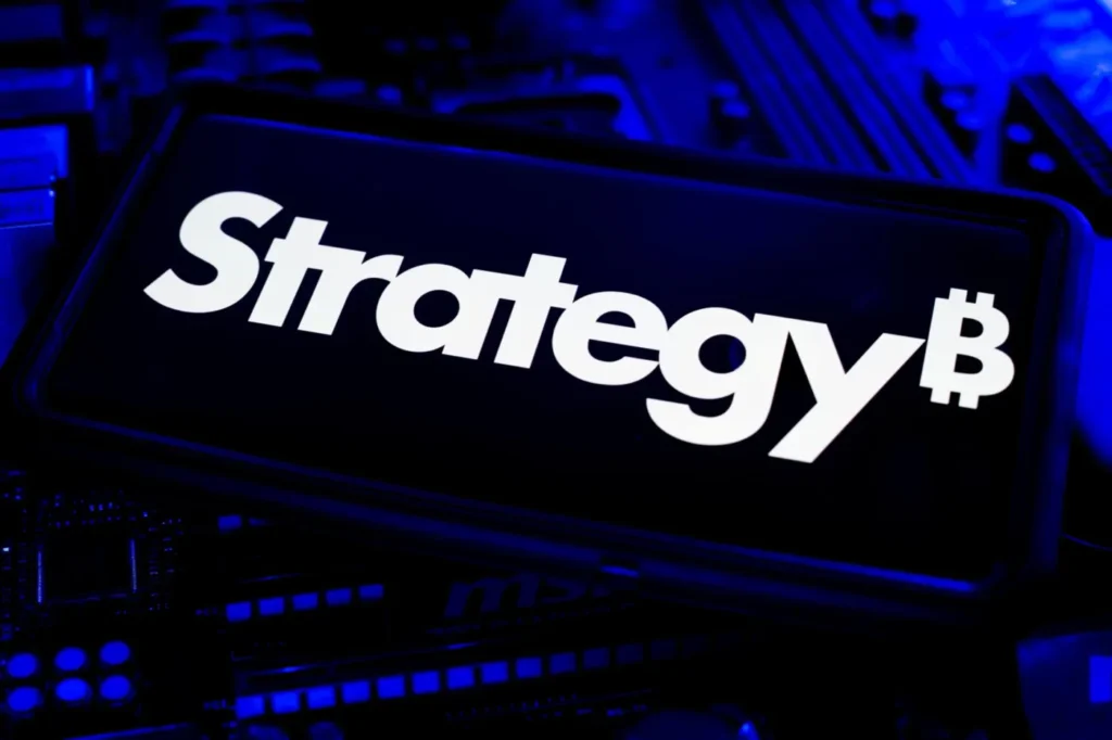 A screen displaying the Strategy₿ logo in bold white text against a dark blue background, with computer hardware and motherboard components visible beneath the display.