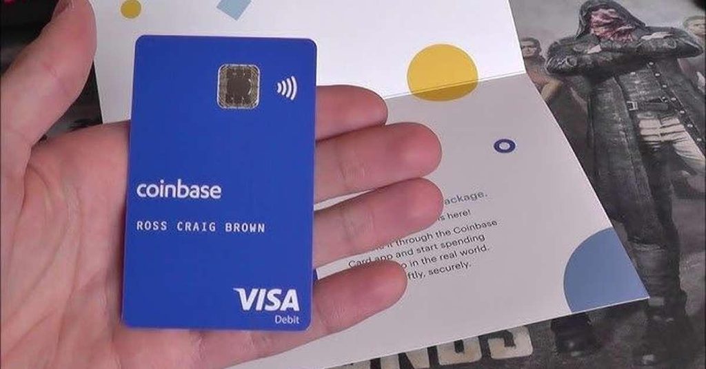 hand holding a blue Coinbase card on top an open card