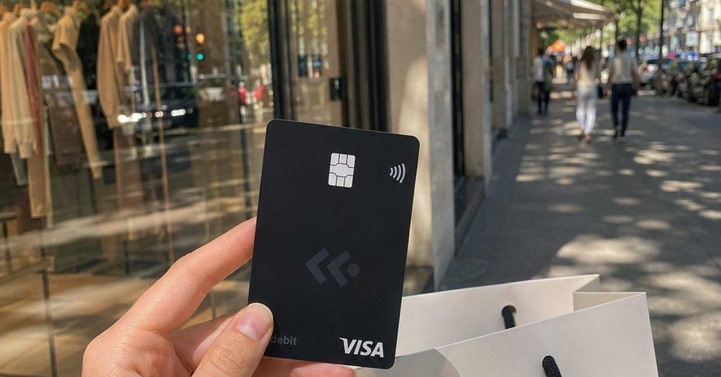 a hand holding the coca card in black color on a walkway with shops