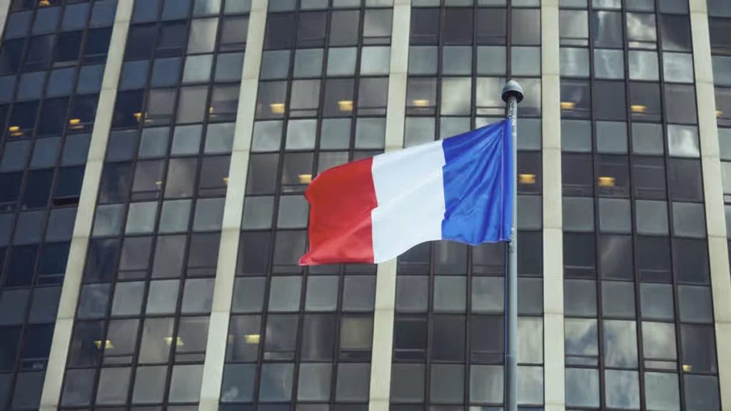 A French flag waving in front of a modern glass office building.