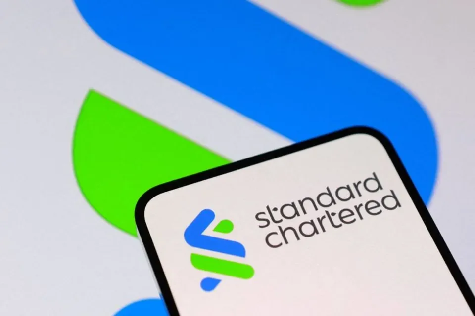 Standard Chartered logo displayed on a smartphone against a white background with blue and green abstract shapes.