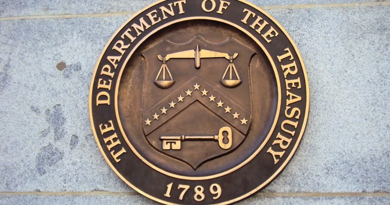 Seal of the U.S. Department of the Treasury mounted on a stone wall, featuring the department's official emblem with scales of justice, a key, and the year 1789.