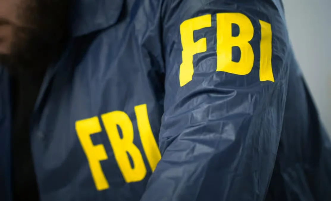 An FBI agent wearing a dark jacket with yellow FBI lettering on the sleeve and chest.