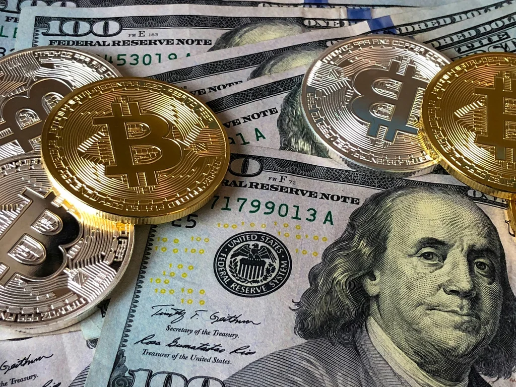 Monedas de Bitcoin sobre billetes de cien dólares estadounidenses.